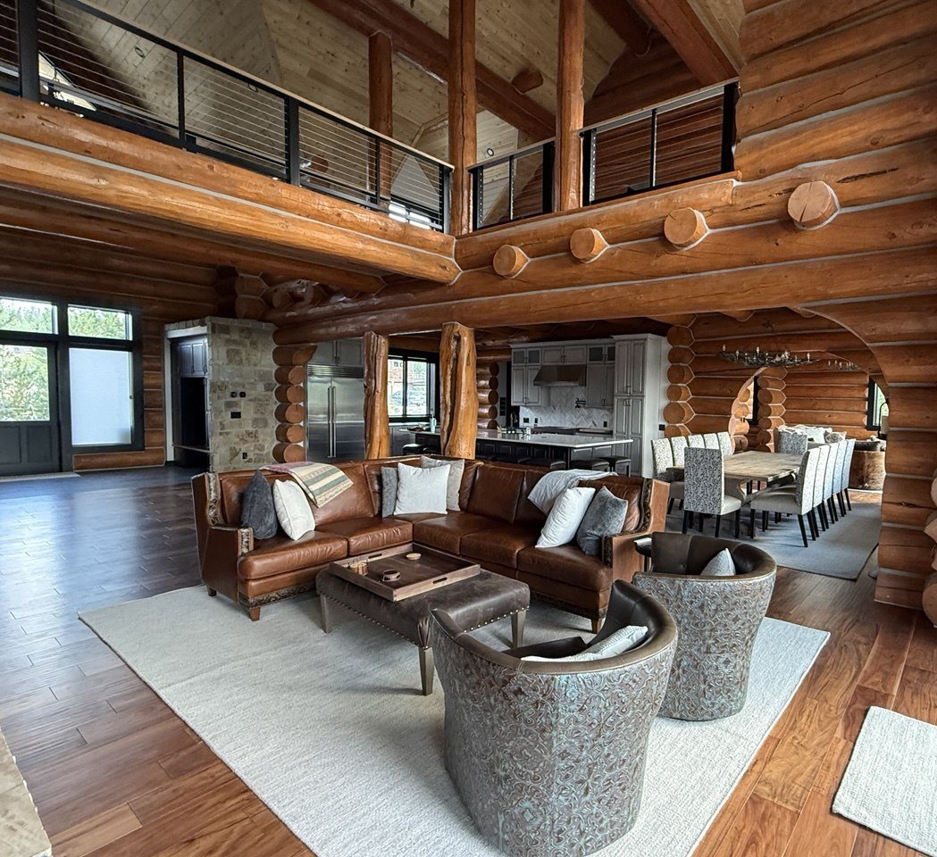 Great room of a log home. Loft, leather, stone, dining under the logs.